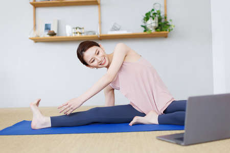 Young Asian woman practicing yoga while watching video on tablet computerの写真素材