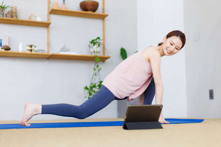 Young Asian woman practicing yoga while watching video on tablet computerの写真素材