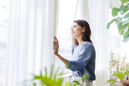 Young Asian woman looking out from the windowの写真素材