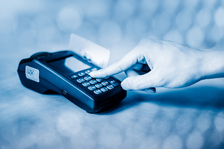 Male hand enters PIN code on wireless POS machine with blue backgroundの写真素材