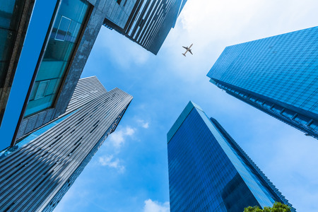 Skyscrapers with a flying airplane against blue sky.の写真素材
