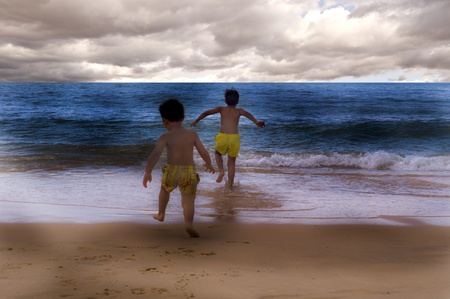 children jumping on beach with cloudy sky in the backgroundの写真素材