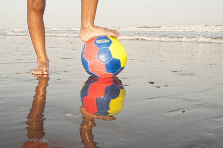 child feet with a ball on the sandy beach