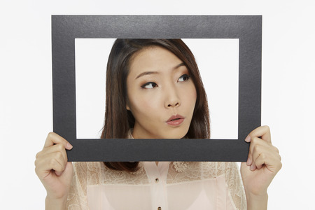 Woman holding up a black picture frame, looking curious