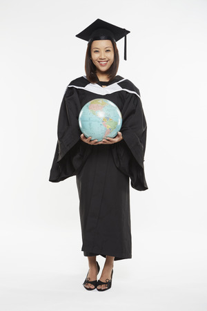 Woman in graduation gown holding a globeの写真素材