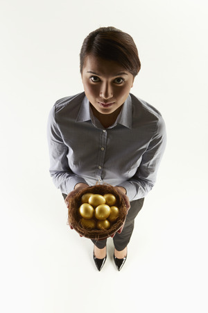 Businesswoman holding a nest filled with golden eggsの写真素材