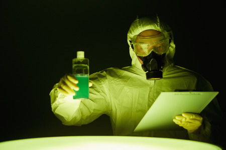 Man in protective suit inspecting a bottle of chemical