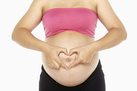 Pregnant woman forming a heart hand gesture against her bellyの写真素材