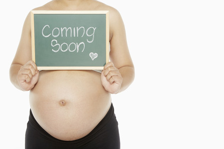 Pregnant woman holding up a blackboard with the words 'Coming Soon written on it"の写真素材