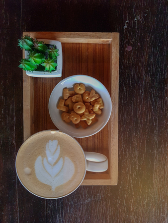 Top view of a mug of coffee and sweets, placed on a wooden tray that is placed on a wooden table in dark brown.の写真素材