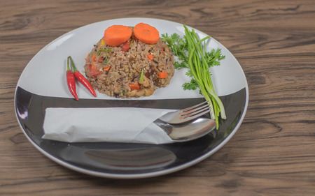 Fried rice with herbs. In a circular plate in black and white. Placed on a wooden table made with rice, fried rice Wright Berry and several types of herbs.の写真素材