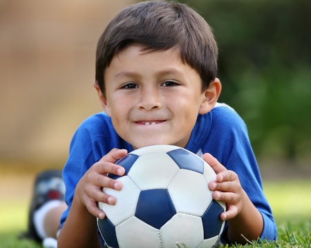 Young brown haired hispanic boy in blue shirt lying down on grass with soccer ball in handsの写真素材