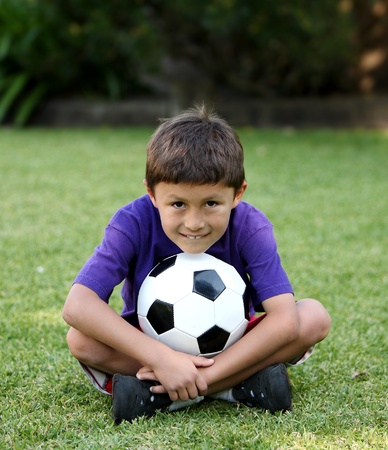 Young Latino boy sitting ion grass with soccer ballの写真素材