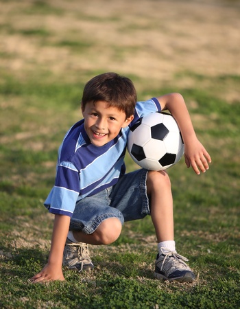Authentic happy Latino boy playing with soccer ball in field wearing blue striped tee shirt.の写真素材