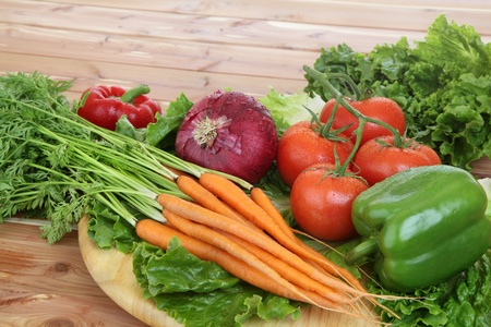 Organic vegetables in rustic setting including tomatoes on the vine, peppers, carrots, lettuce.