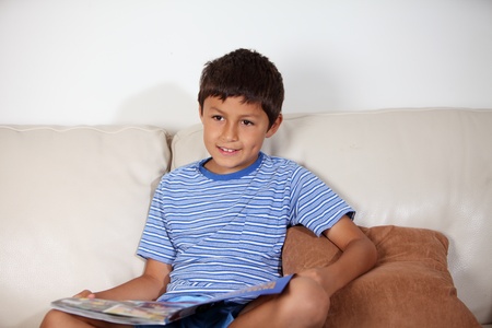 Young boy on the sofa reading a magazineの写真素材