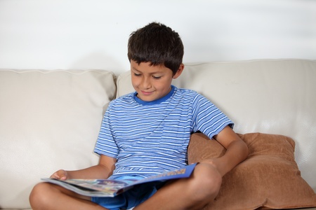 Young boy on the sofa reading a magazineの写真素材
