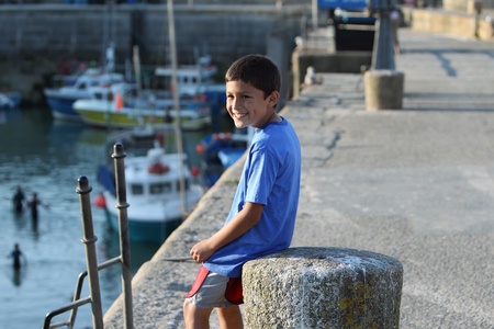 Young Hispanic boy smiles while sitting on a concrete bollard on an old harbor wallの写真素材