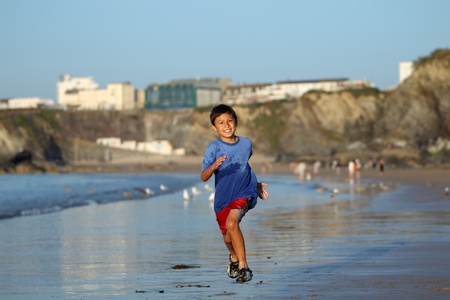 Young boy plays and runs in the surf along an English beach near sunsetの写真素材