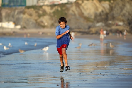 Young boy plays and runs in the surf along an English beach near sunsetの写真素材