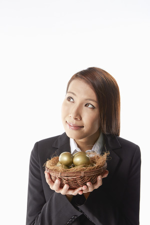 Businesswoman carrying a nest filled with gold eggsの写真素材