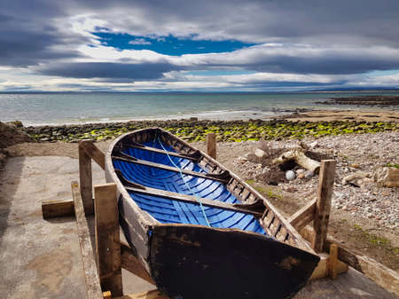a blue fishing boat on the shore of the North Sea with a spectacular skyの写真素材