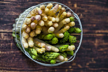 new harvest of German white and green asparagus, bunch of raw green and white asparagus in basket with background of woodの写真素材