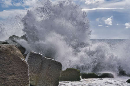 Turquoise wave breaking on a beach in sea with silver cloudsの写真素材