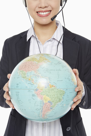 Businesswoman with headset holding a globeの写真素材
