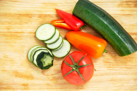 cutting circles zucchini, red tomato, red pepper and yellow, on a wooden boardの写真素材