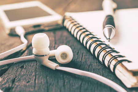 White headphones, smartphone with notebook on wood table background vintage color.の写真素材