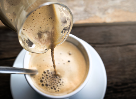 pouring coffee into cappuccino cup on the retro wooden table background.の写真素材