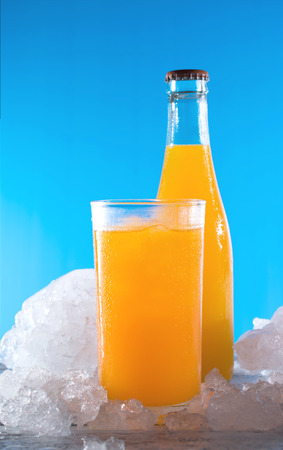 bottle of orange soda with glass and ice on a wood table.の写真素材