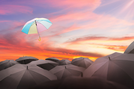 abstract umbrella flying over many black umbrellas with beautiful sky, leadership background concept.の写真素材
