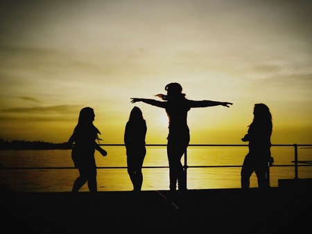 The silhouettes of a group of happy people enjoying the scenic view of the ocean, at sunsetの写真素材