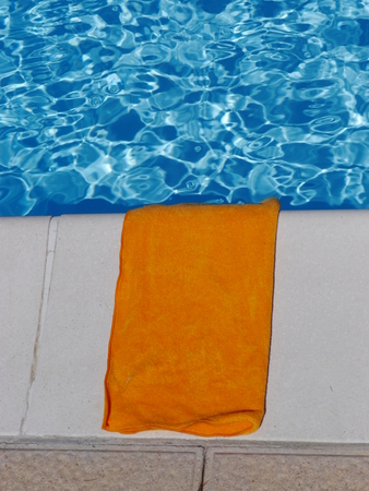 a towel is laying by clear blue waterの写真素材