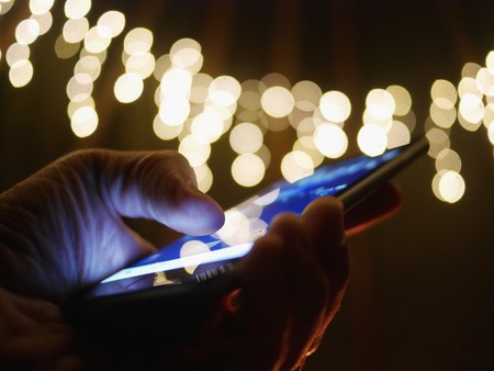 Using cellphone at night - with defocused city lights in the background.の写真素材