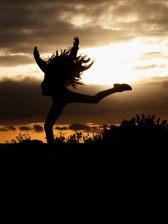 Silhouette of a beautiful girl jumping over sunset