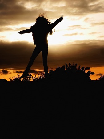Silhouette of a beautiful girl jumping over sunsetの写真素材