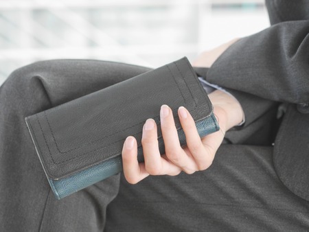 close-up of unrecognizable elegant female in suit sitting with black leather wallet in handの写真素材