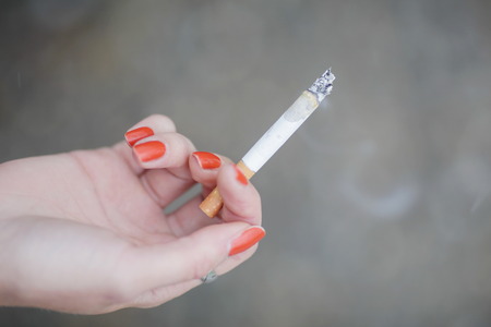 Close-up of female hand with red manicure holding smoking cigaretteの写真素材