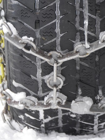 Close-up of frozen car tyre fasten with chain, covered with icicles.