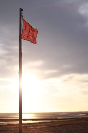 Red flag is flying on a pole in front of a cloudy skyの写真素材