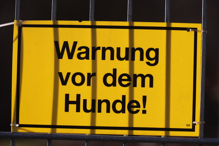 A yellow sign with black writing that says "Warning: Vor dem Hunde!" is hangingの写真素材