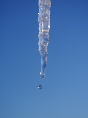 A drop of water is falling from a frozen icicle