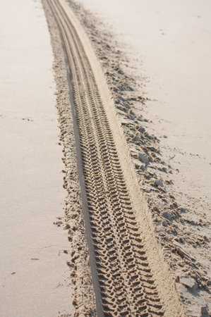 Tire track is visible on the sand, leading to a beach