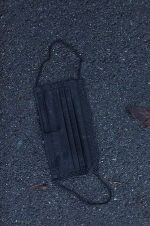 A black disposable face mask is laying on the groundの写真素材