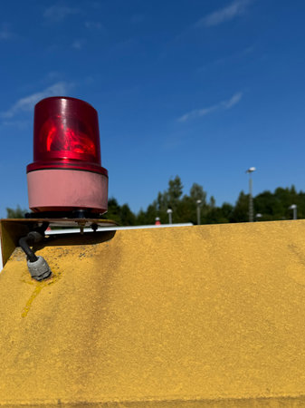 A Red Warning Light is displayed on a Yellow Surface beneath a Clear Blue Sky backdropの写真素材