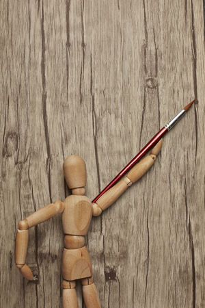 Wooden mannequin holding paintbrush with wooden backgroundの写真素材