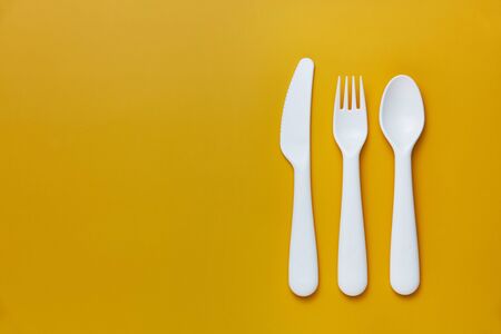 Plastic white cutlery set with yellow background. Top viewの写真素材